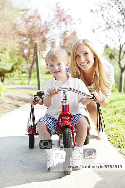 Mother and son (2-3) riding on tricycle in park