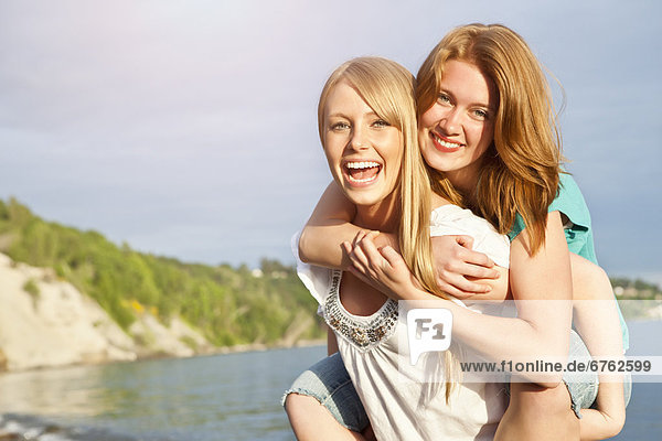 Portrait of two young women piggy-backing on beach