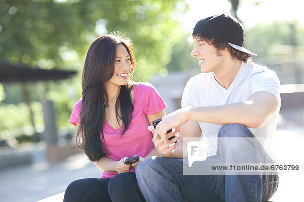 Young multi-racial couple sitting together playing with their mobile phones