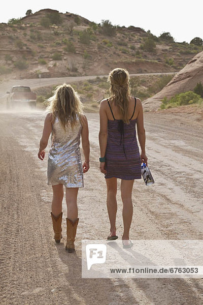 Two young women walking on dirt track in desert