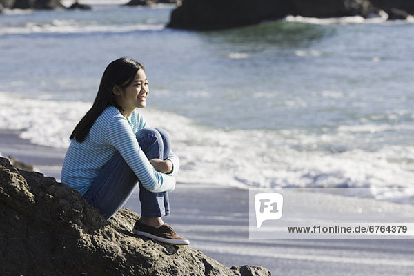 Teenage girl sitting on coastal rock