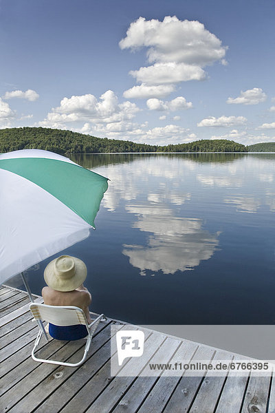 Woman sitting under umbrella on dock  Smoke Lake  Algonquin Park  Ontario