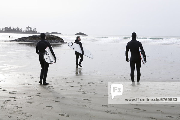 Three Surfers Walk on Beach Toward the Surf  Tofino  British Columbia