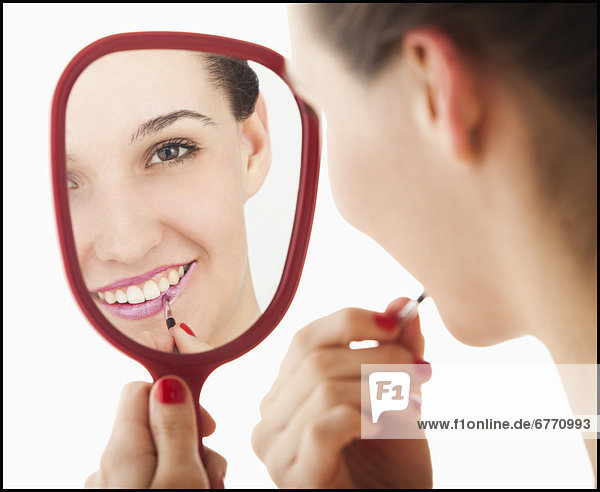 Studio portrait of young woman applying lipstick in mirror