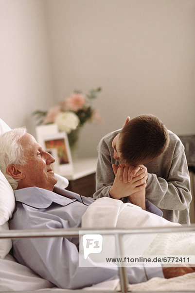 Grandfather lying in hospital bed as his grandson holds his hand