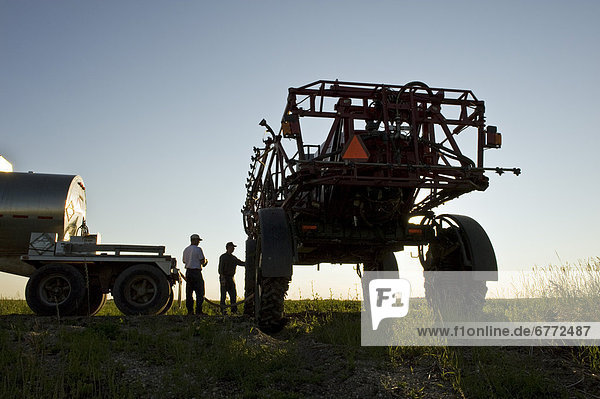 Two farmers load a high clearance sprayer with chemical fungicide and water from a nurse truck  near Dugald  Manitoba