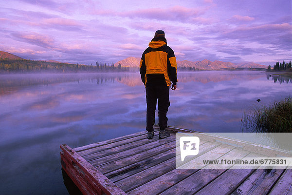 Hiker Standing on a Dock at Sunrise  Jackfish Lake  near the confluence of the North Canol and Robert Campbell Highways  south of Ross River  Yukon