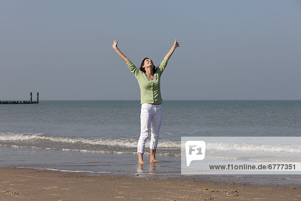 Woman standing on beach with arms raised