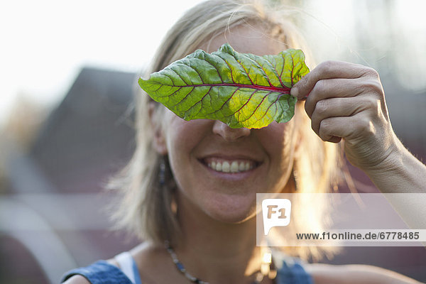 Smiling woman holding leaf in front of her face