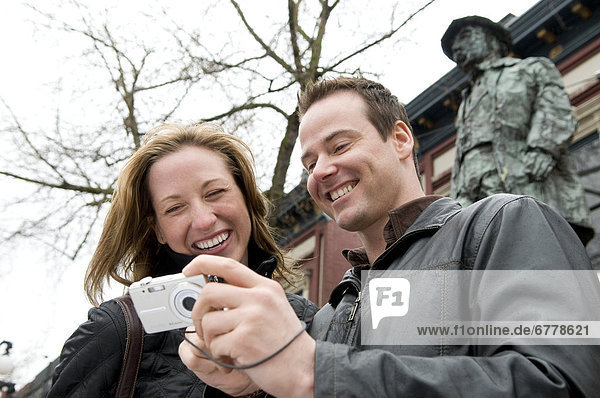 Couple Laughing at Photo they Took Standing front of Statue of Gassy Jack in Historic Gastown  Vancouver  British Columbia