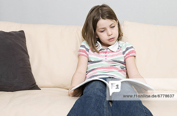 Girl (6-7) reading book on sofa