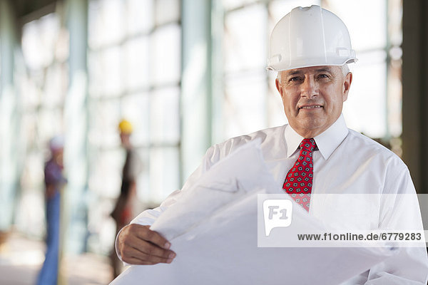 Portrait of senior man wearing tie and hardhat  holding blueprint