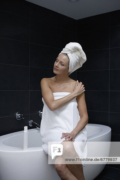 Mature woman sitting in bathroom wrapped in towel
