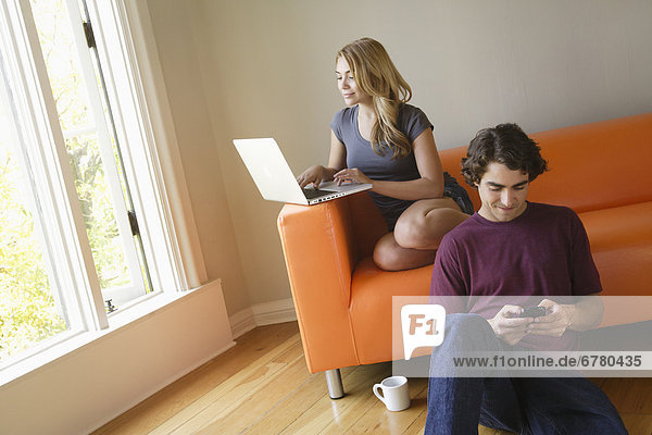 Young couple in living room  using phone and laptop
