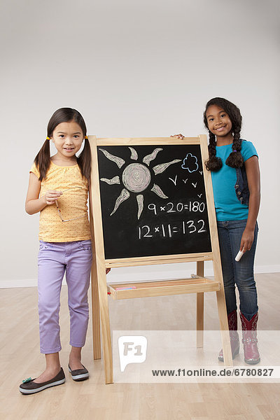 Studio portrait of two girls (8-9) standing by blackboard