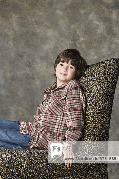 Portrait of boy (6-7) sitting on chair with animal print  studio shot
