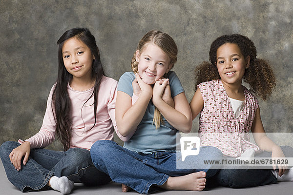 Portrait of three smiling girls (8-9) sitting together  studio shot