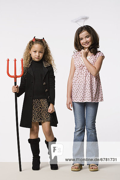 Studio portrait of two girls (8-9) wearing Halloween costumes with trident and halo