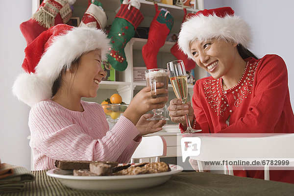 Mother and daughter wearing santa hats toasting with drinks