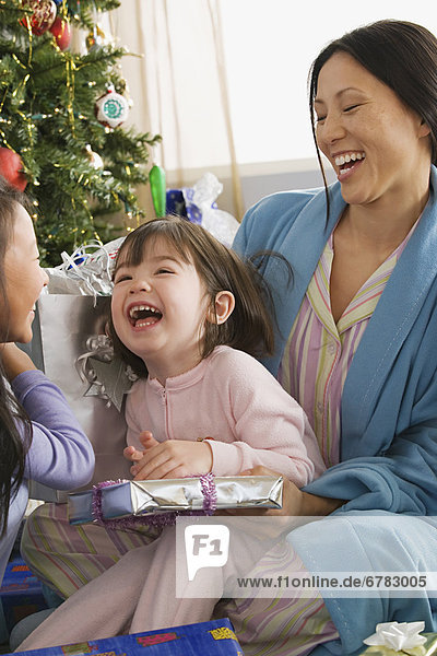 Mother and daughters (10-11) unwrapping christmas gifts
