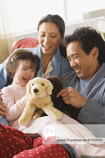 Parents and daughter sitting in bed and playing with stuffed toys
