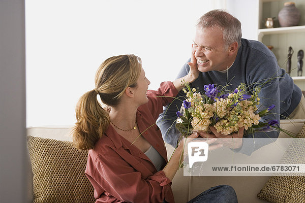 Senior man giving flowers to woman sitting on sofa
