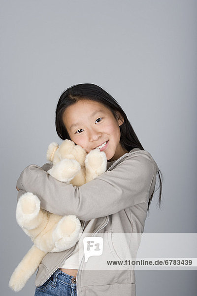 Studio portrait of teenage Chinese girl (16-17) hugging teddy bear