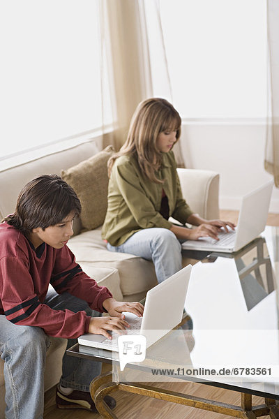 Brother and sister using laptops in living room