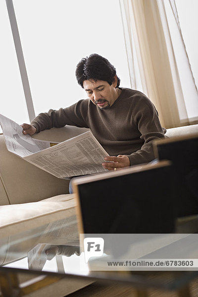 Mature man reading newspaper in living room