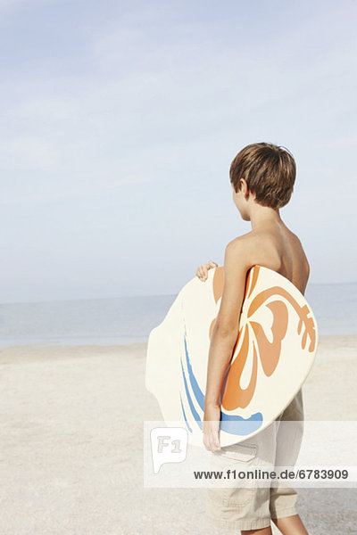 Boy holding skimboard on beach