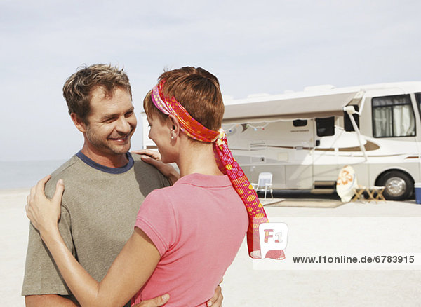 Couple hugging by motor home on beach