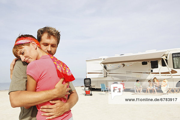 Couple hugging on beach with motor home in background