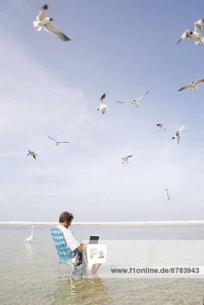 Man sitting in ocean surf with laptop