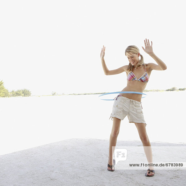 Young woman hula hooping on beach
