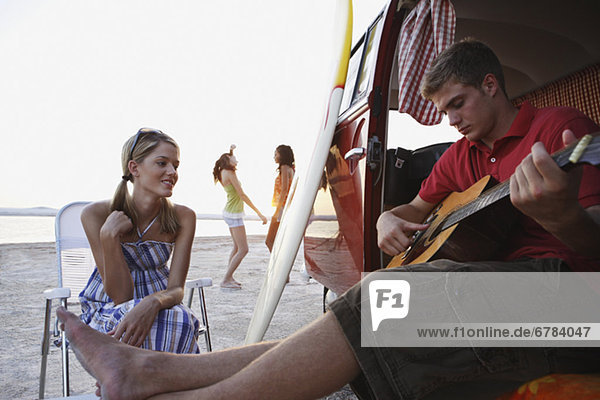 Man playing guitar in van on beach