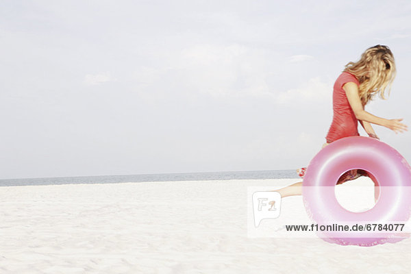Teenage girl rolling inflatable ring on beach