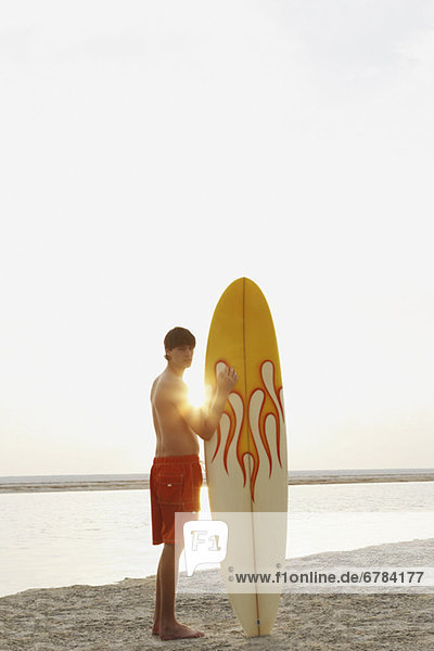 Teenage boy standing with surfboard on beach