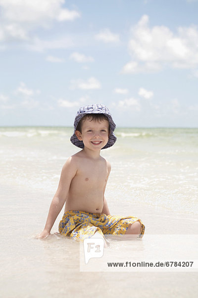 Boy sitting in shallow ocean