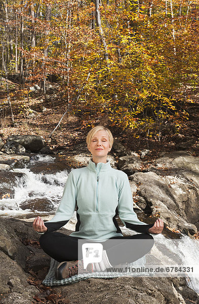 Woman meditating by stream in forest