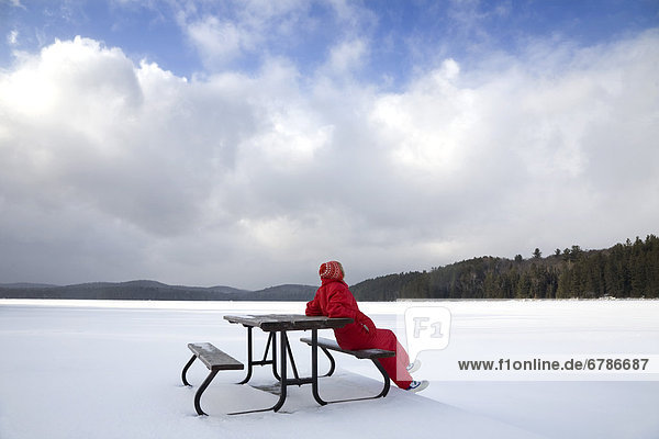 Senior woman sitting on a picnic table in snow by a frozen lake  Algonquin Park  Ontario