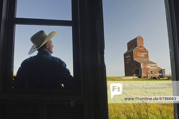 Farmer looking towards an abandoned grain elevator  in the ghost town of Bents  Saskatchewan