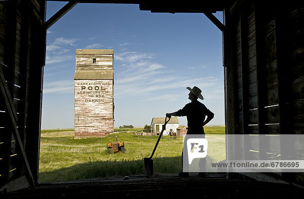Farmer with a shovel looking out at an abandoned grain elevator  Dankin  Saskatchewan