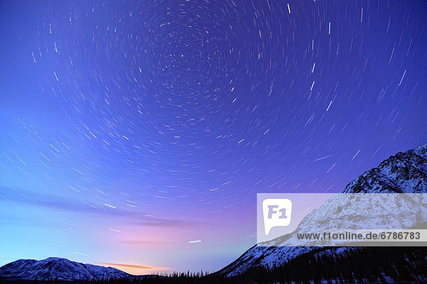 Star trails above a mountain with northern lights on horizon  Yukon