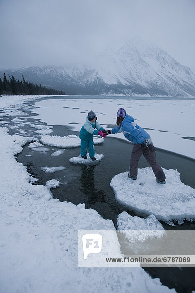 Girl helping sister across ice floes on freezing Lake  Kathleen Lake  Kluane National Park  Yukon Territory  Canada