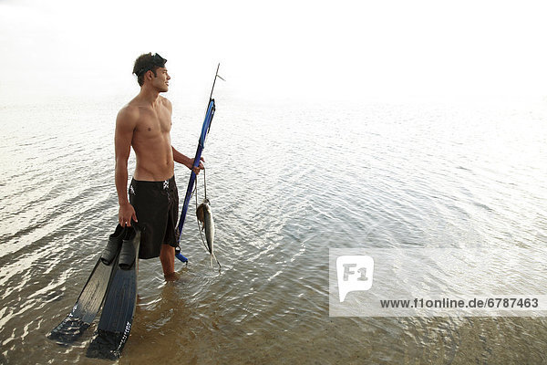 Hawaii  Oahu  Mann  hält seine Speargun  Flossen und Fisch fing an ein String steht im Wasser.