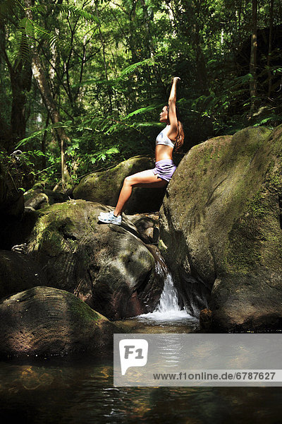 Hawaii  Oahu  Young female doing yoga in a lush forest with waterfall below her.