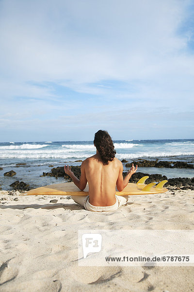 Hawaii  Oahu  junger Mann am Strand Meditieren mit Surfboard.
