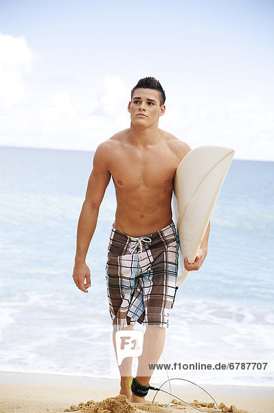 Hawaii  Kauai  Haena Beach  young man at the beach walking with surfboard.