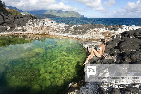 Hawaii  Kauai  Princeville  Queens Bath  Attractive woman sitting on rocks.