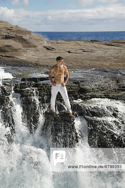 Hawaii  Oahu  Male wearing white pants on rocky cliff.